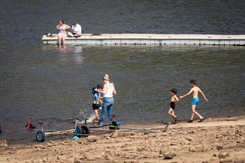 People enjoying a sandy lakeside, with a rowing boat on the water