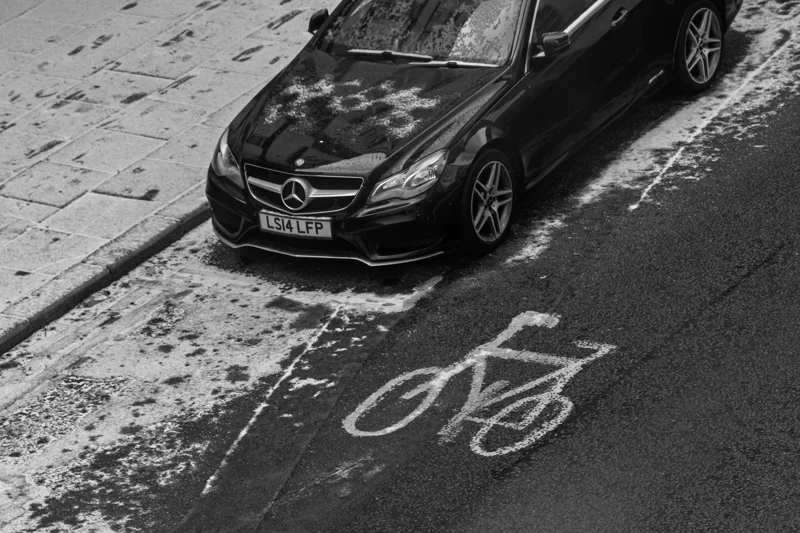 A car beside a bicycle lane marking, photographed from above in black and white