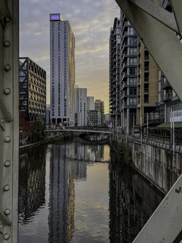 City buildings reflected in a canal, framed by a bridge structure